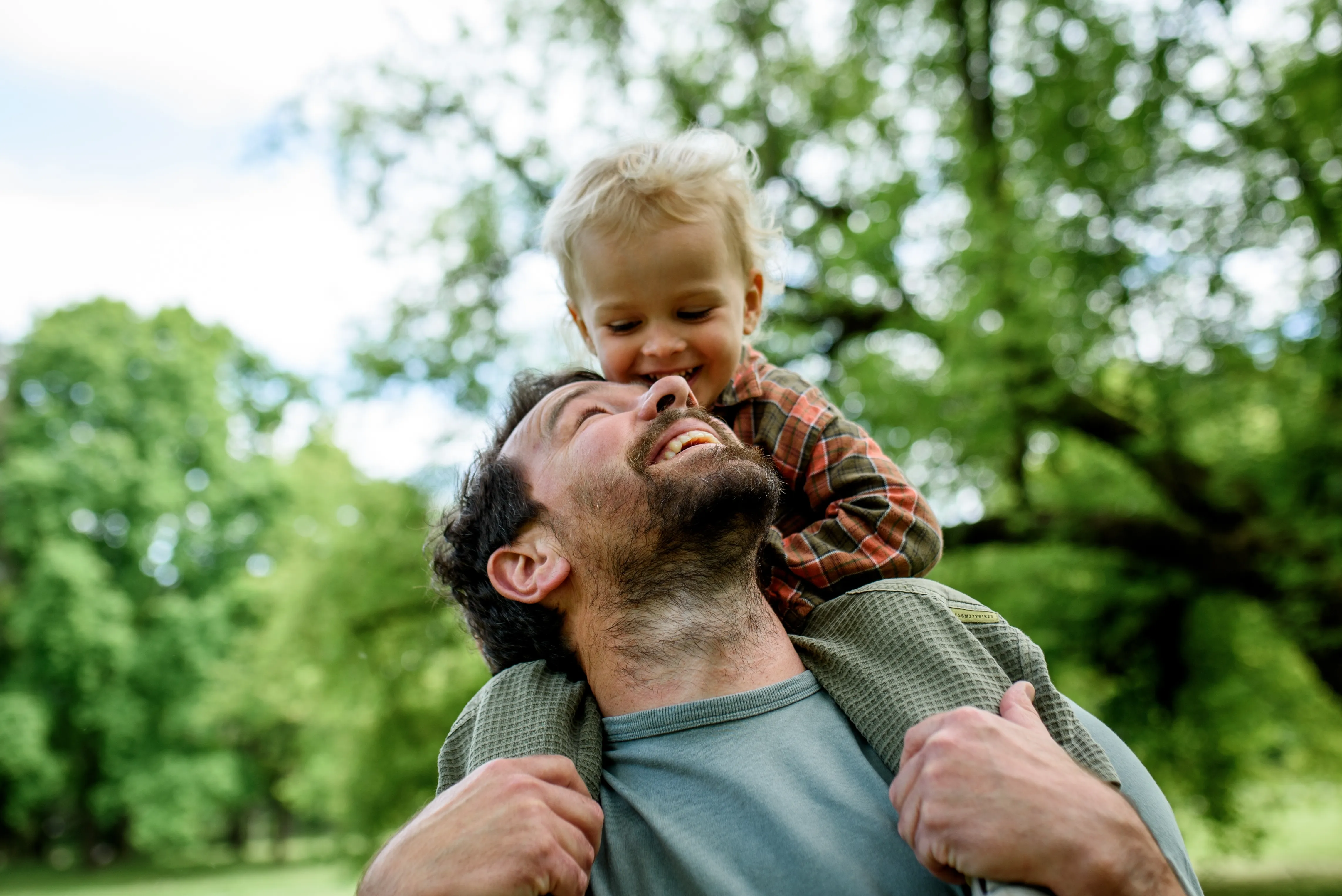 A father lifting his young child on his shoulders, both laughing